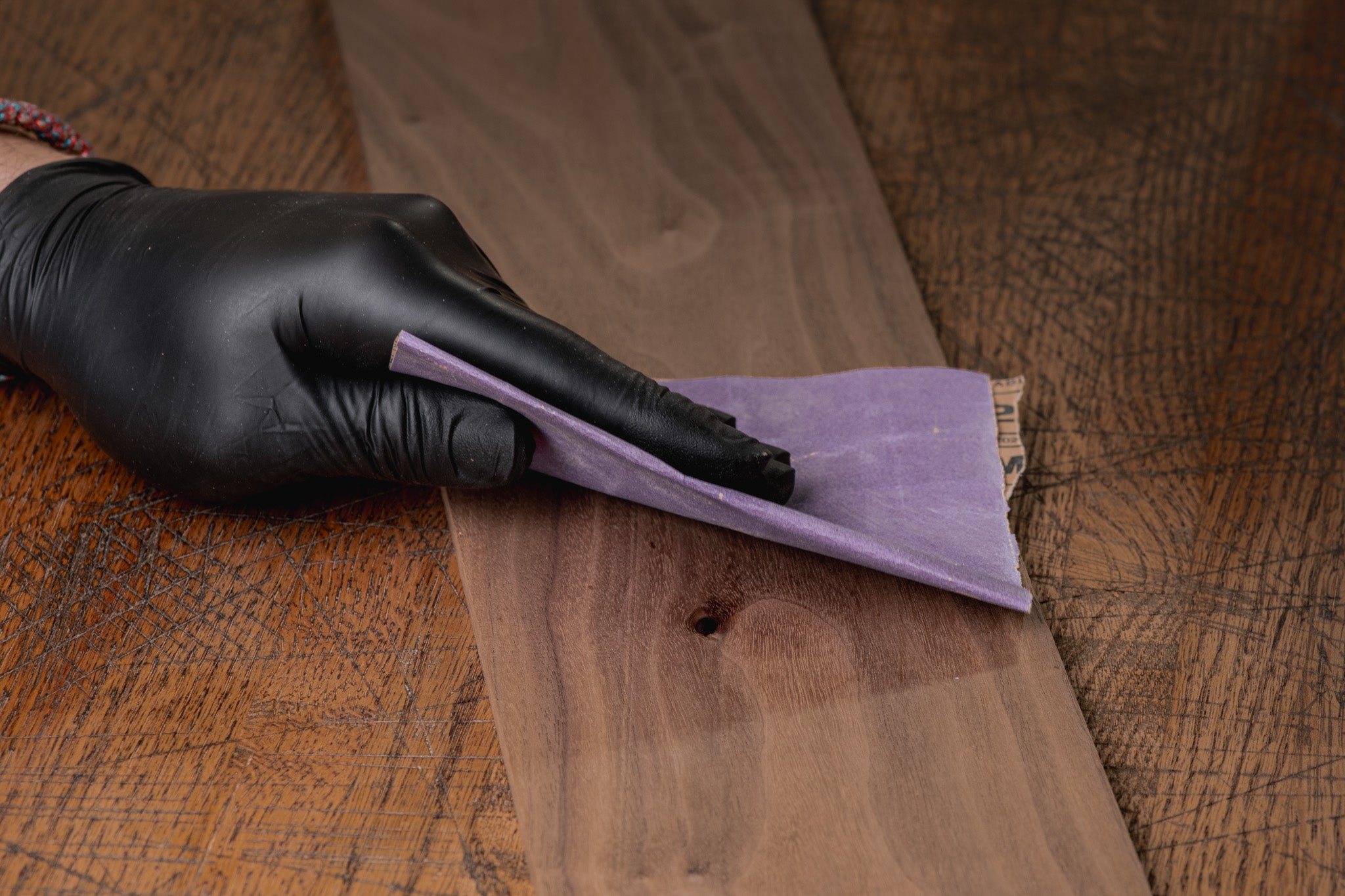 Person wearing black gloves sanding a wooden surface with a purple sanding block.