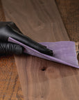 Person wearing black gloves sanding a wooden surface with a purple sanding block.