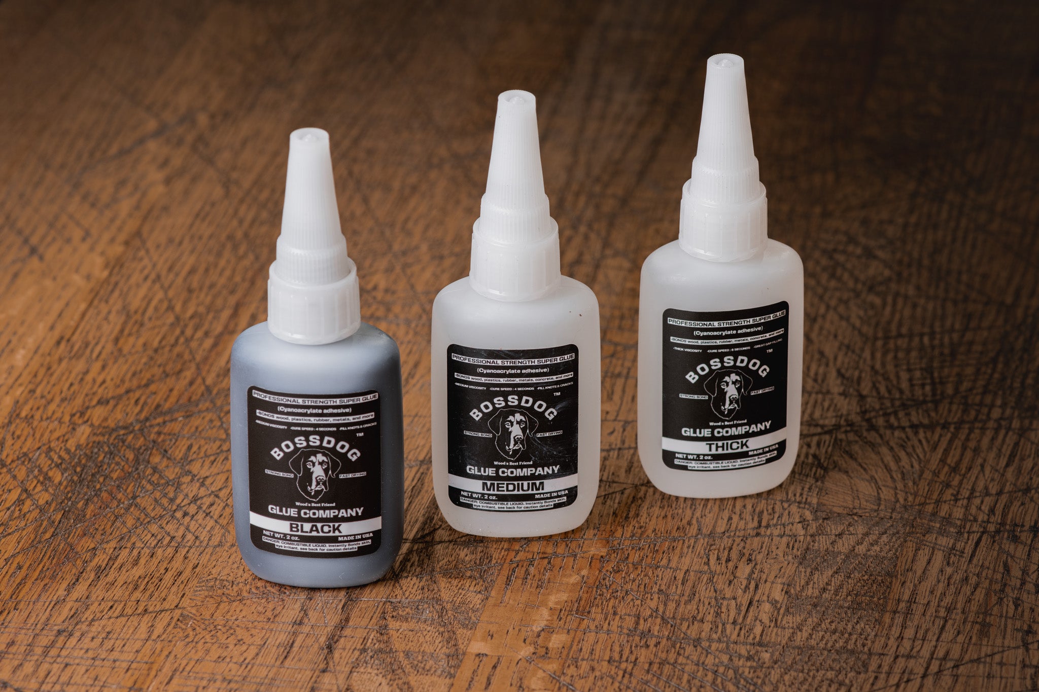 Three bottles of BOSSDOG Glue Company products on a wooden surface